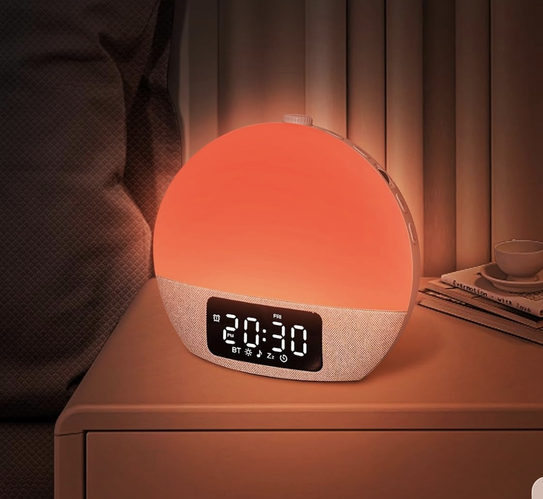 Pink-orange sunrise alarm clock glowing on a bedside table
